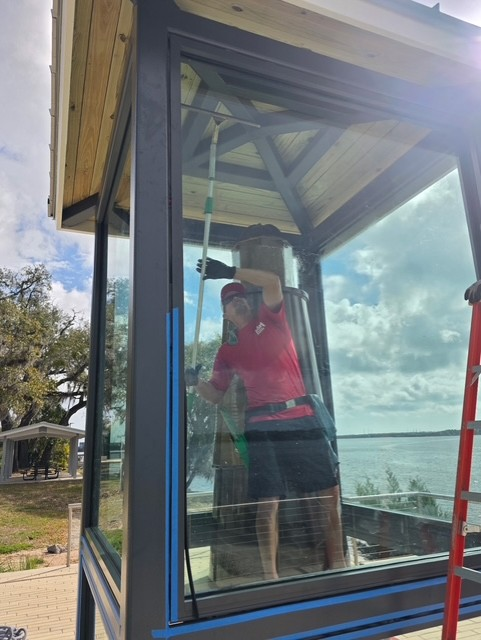 Man in red FISH Window Cleaning shirt holing a squeegee cleaning the enclosure at El Faro Memorial at Dames Point Park.