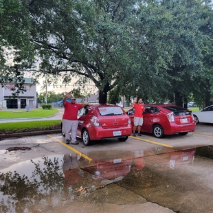 two fish employees standing next to two red fish window cleaning cars