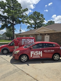 fish employee standing in between red fish window cleaning car and red fish window cleaning van