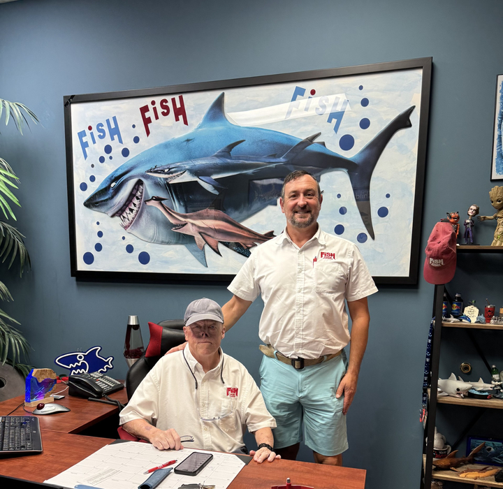 one man sitting at desk, one man standing next to him